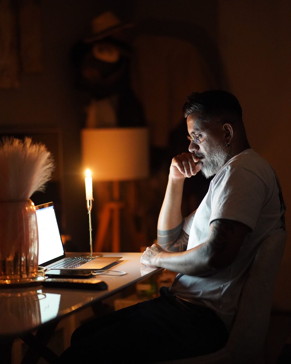 A man alone at a laptop late at night, a candle on the desk